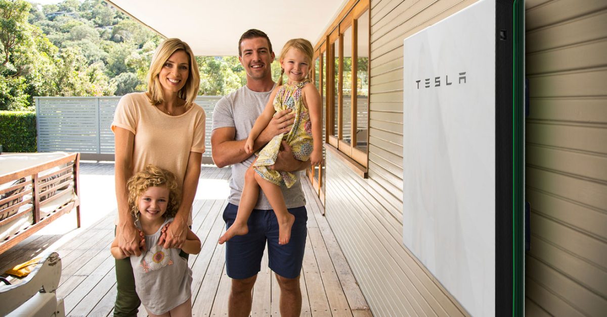 Family with two kids standing next to Tesla Powerwall